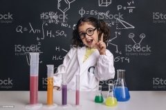 funny scientist child with glasses in lab coat with chemical flasks having an idea, school blackboard background with hand drawn science formulas, back to school and successful female career concept