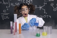 funny scientist girl with gloves and goggles in lab coat mixing chemical flasks, blackboard background with science formulas, explosion in the laboratory, back to school concept