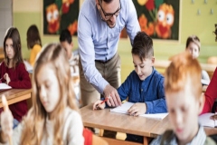 Happy male teacher assisting his student on a class at elementary school.